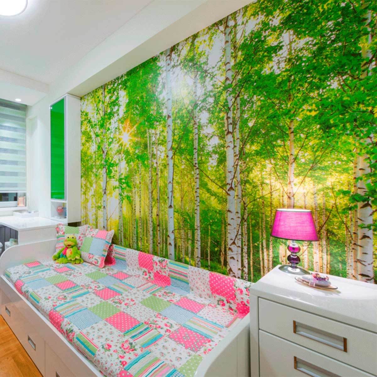 A brightly colored patchwork bed with plush pillows sits against a nature-themed wall mural of trees, illuminated by a pink lamp in a cozy room.