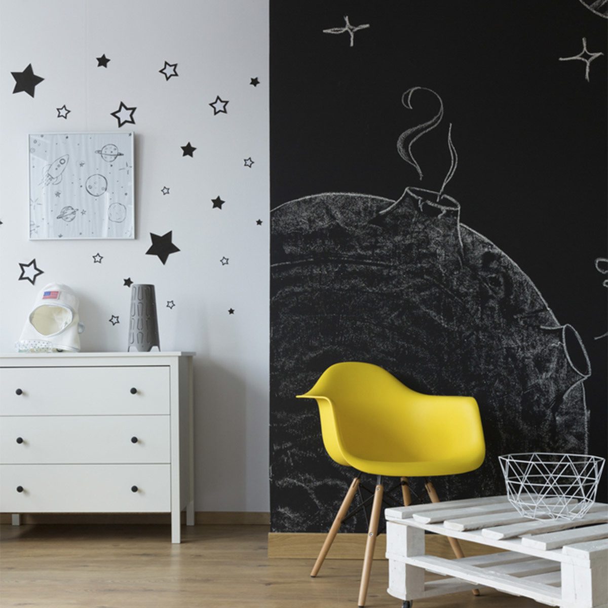 A yellow chair sits next to a white wooden table in a room featuring a black wall with a planet design and star decorations.
