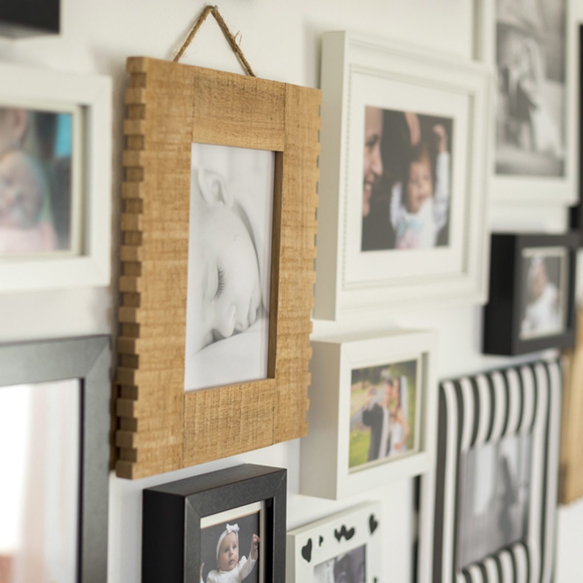 A wooden photo frame displays a sleeping baby image, hanging on a wall adorned with various framed photographs in contrasting colors and styles.