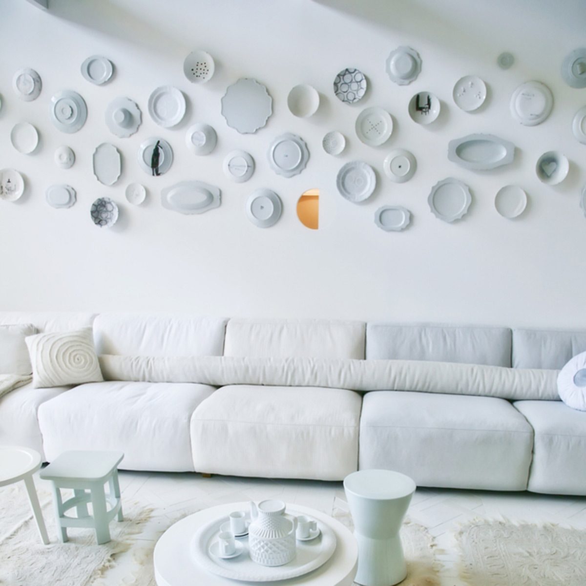 A white sofa sits against a wall adorned with various decorative plates, while a small coffee table holds a porcelain set, creating a serene living space.