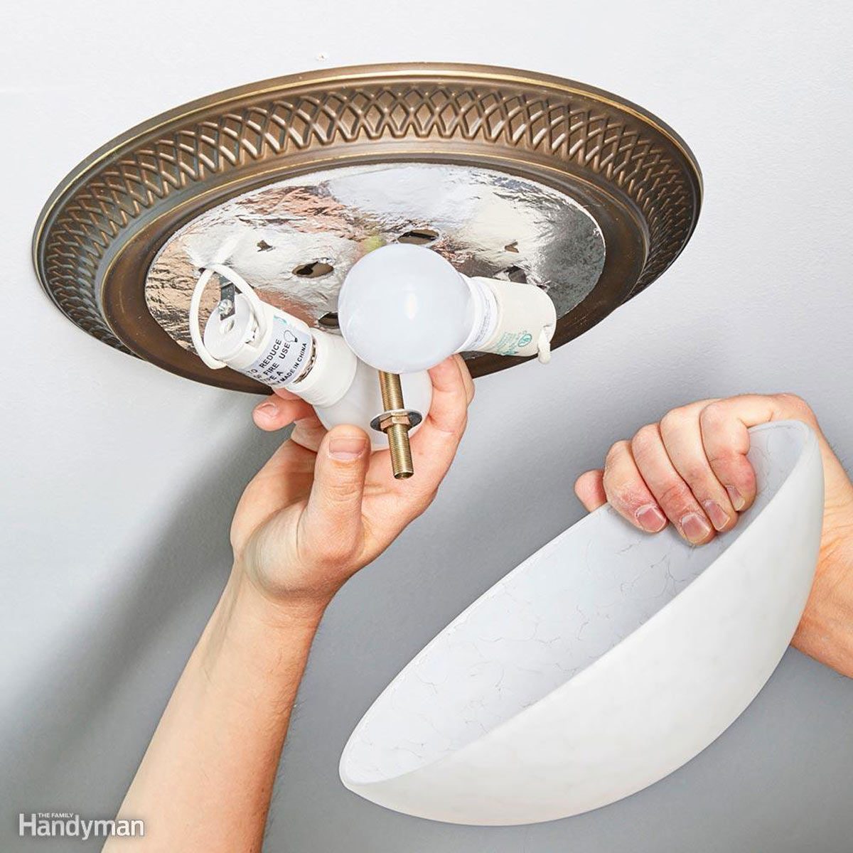 A person is installing a light fixture by attaching it to a ceiling plate, surrounded by a plain ceiling in a well-lit environment.