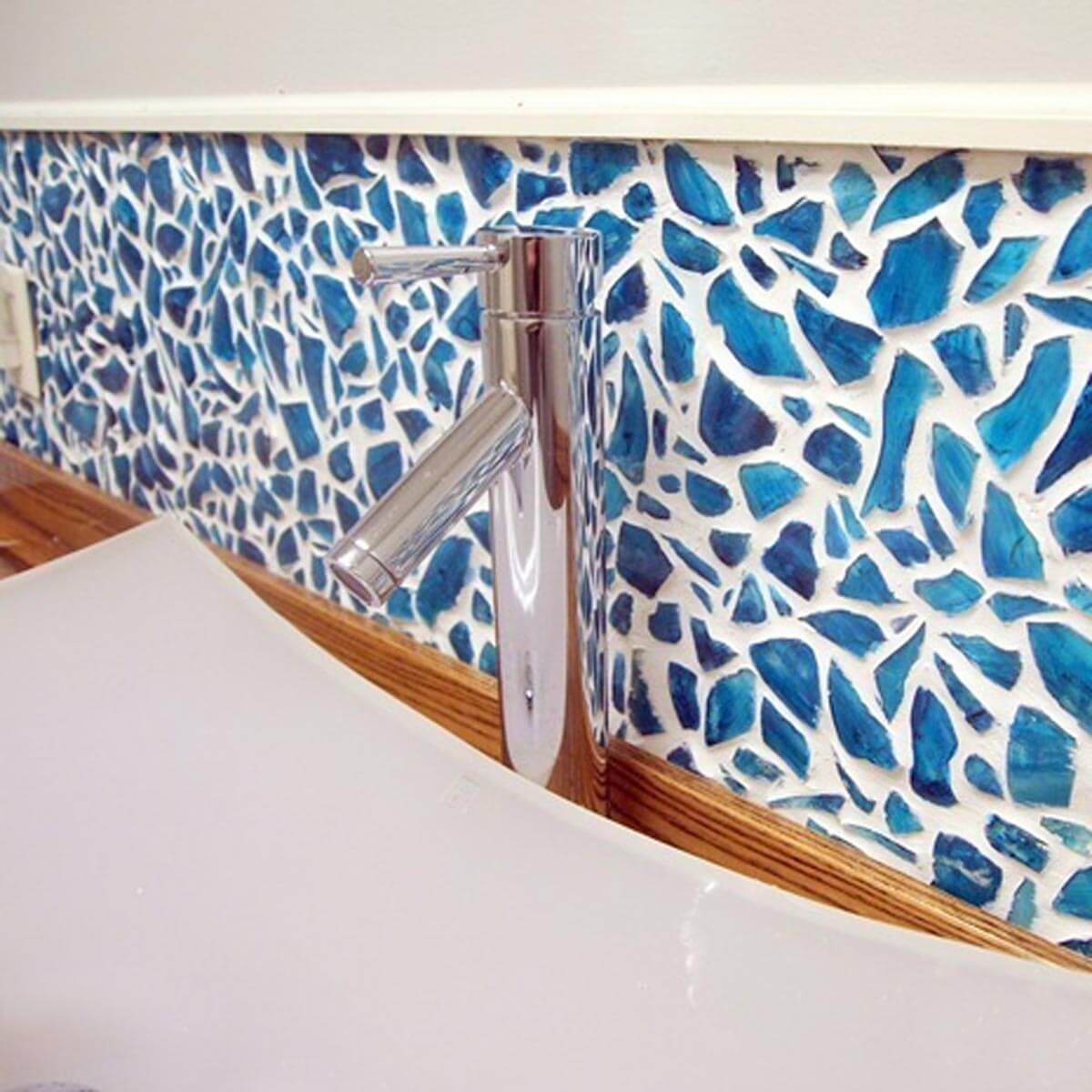 A chrome faucet stands over a smooth, curved white sink, against a blue and white decorative stone wall, creating a modern bathroom aesthetic.