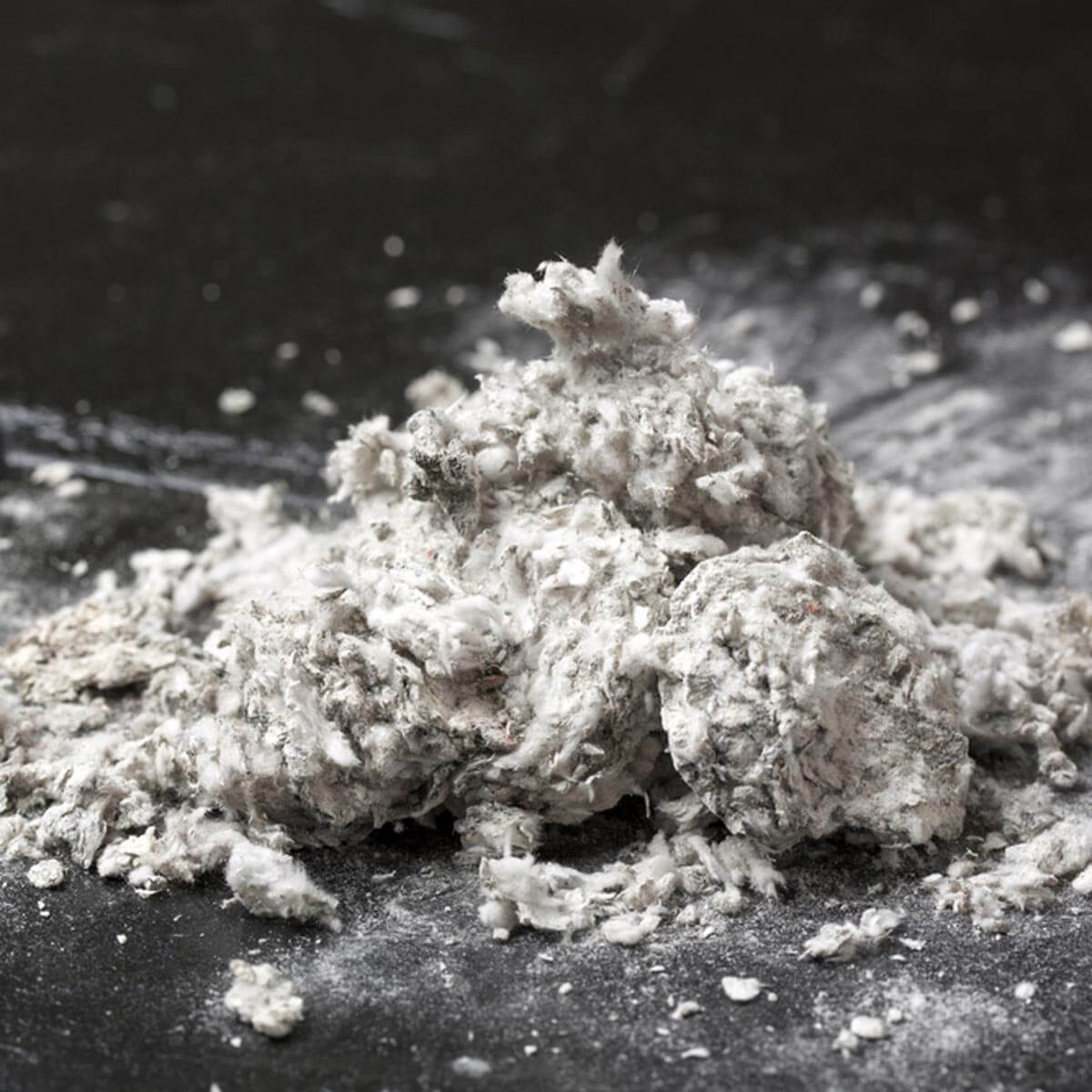 A pile of loosely packed, light-colored fibers sits on a dark surface, with some fibers scattered nearby, suggesting recent disturbance or movement.