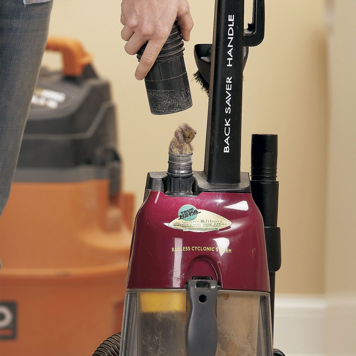 A hand holds a vacuum attachment while removing a hairball from the vacuum's nozzle, set against a clean, indoor space.