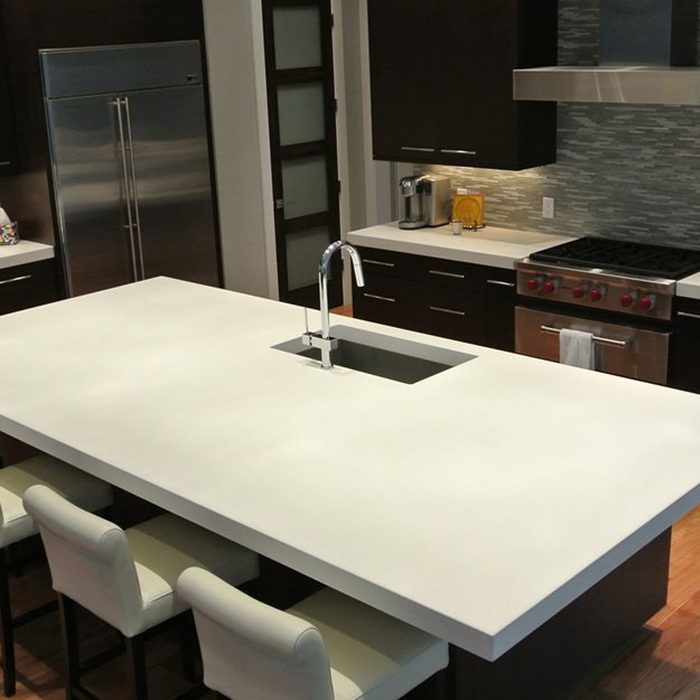 A large white kitchen island with a sink creates a central workspace, surrounded by modern dark cabinetry and stainless steel appliances in a contemporary setting.