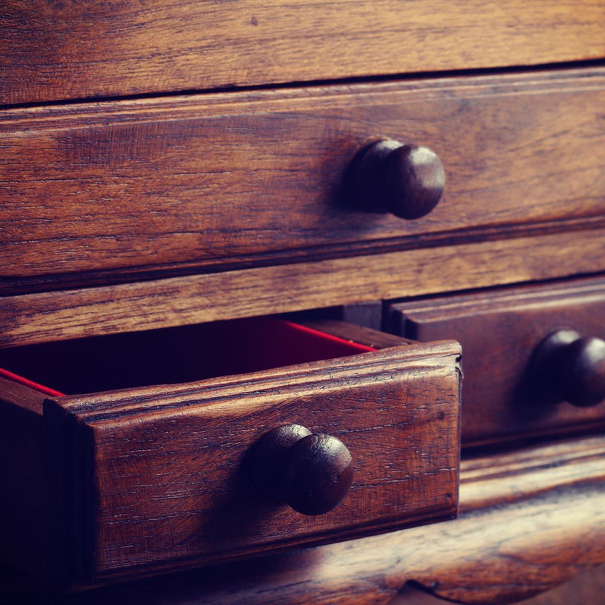 A wooden dresser with several drawers, one slightly open revealing a red interior. The surface has a smooth, vintage finish.