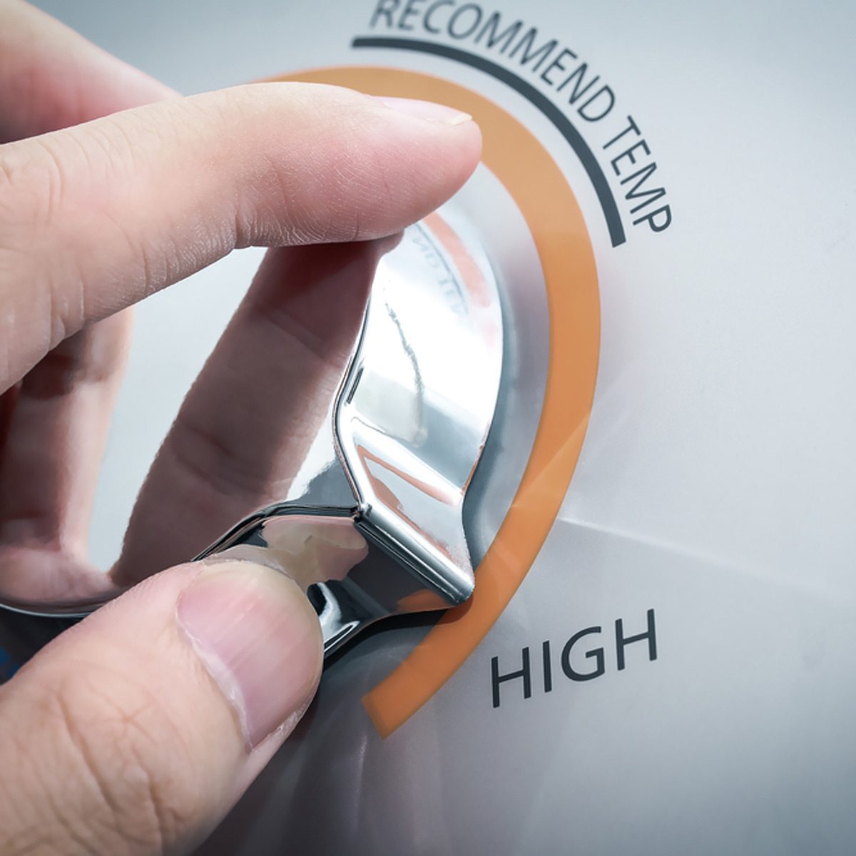 A hand adjusts a metallic dial on a device, moving it towards the "HIGH" setting in a kitchen environment.