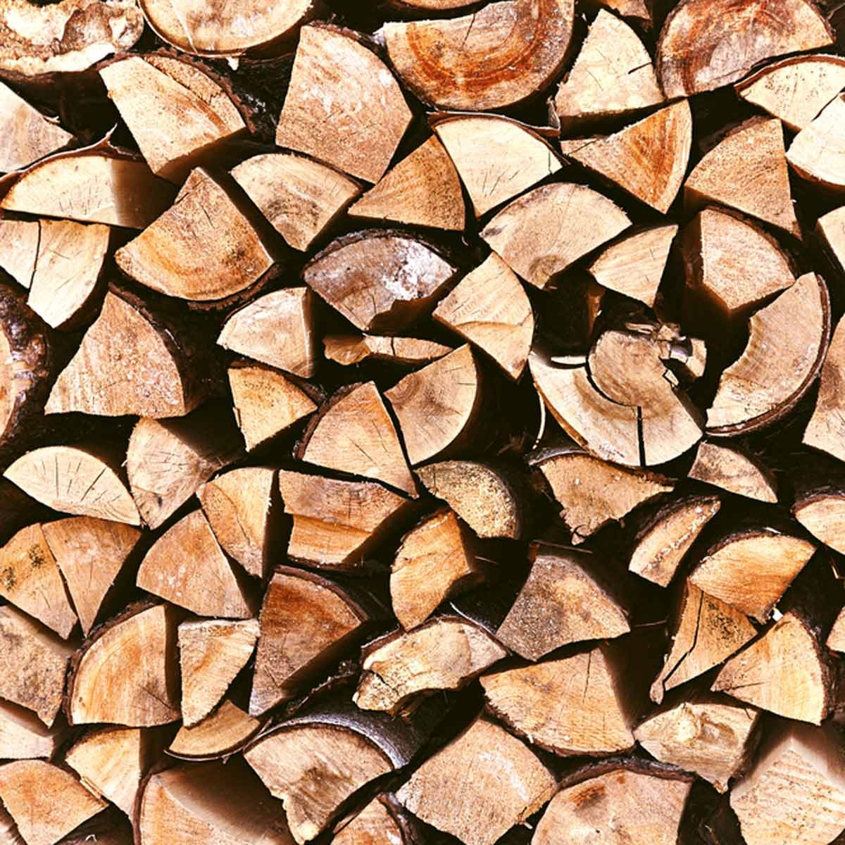 A pile of neatly stacked, cut logs displays their textured surfaces and varied shapes, indicating they are prepared for use, possibly for firewood or construction.
