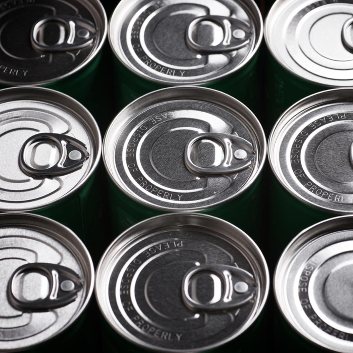 A group of metal beverage cans is arranged closely, displaying their opening tabs on top, set against a muted background.