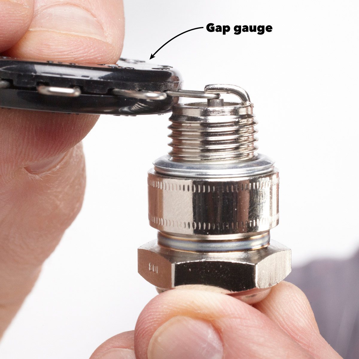 A hand holds a spark plug while a gap gauge measures the gap, against a plain background.