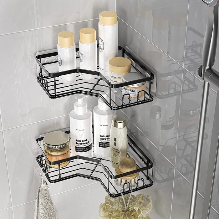 A black wire shower caddy holds various bottles and jars, organized on two levels, against a tiled wall, with a bath sponge hanging below.