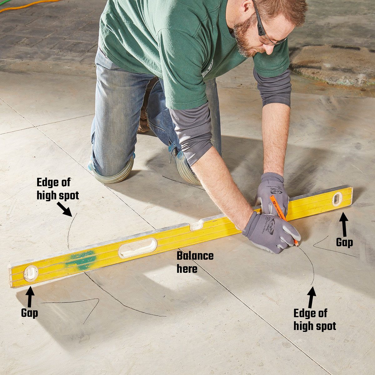 A person kneels on a concrete floor, using a leveling tool to mark gaps and high spots while preparing for a flooring adjustment.