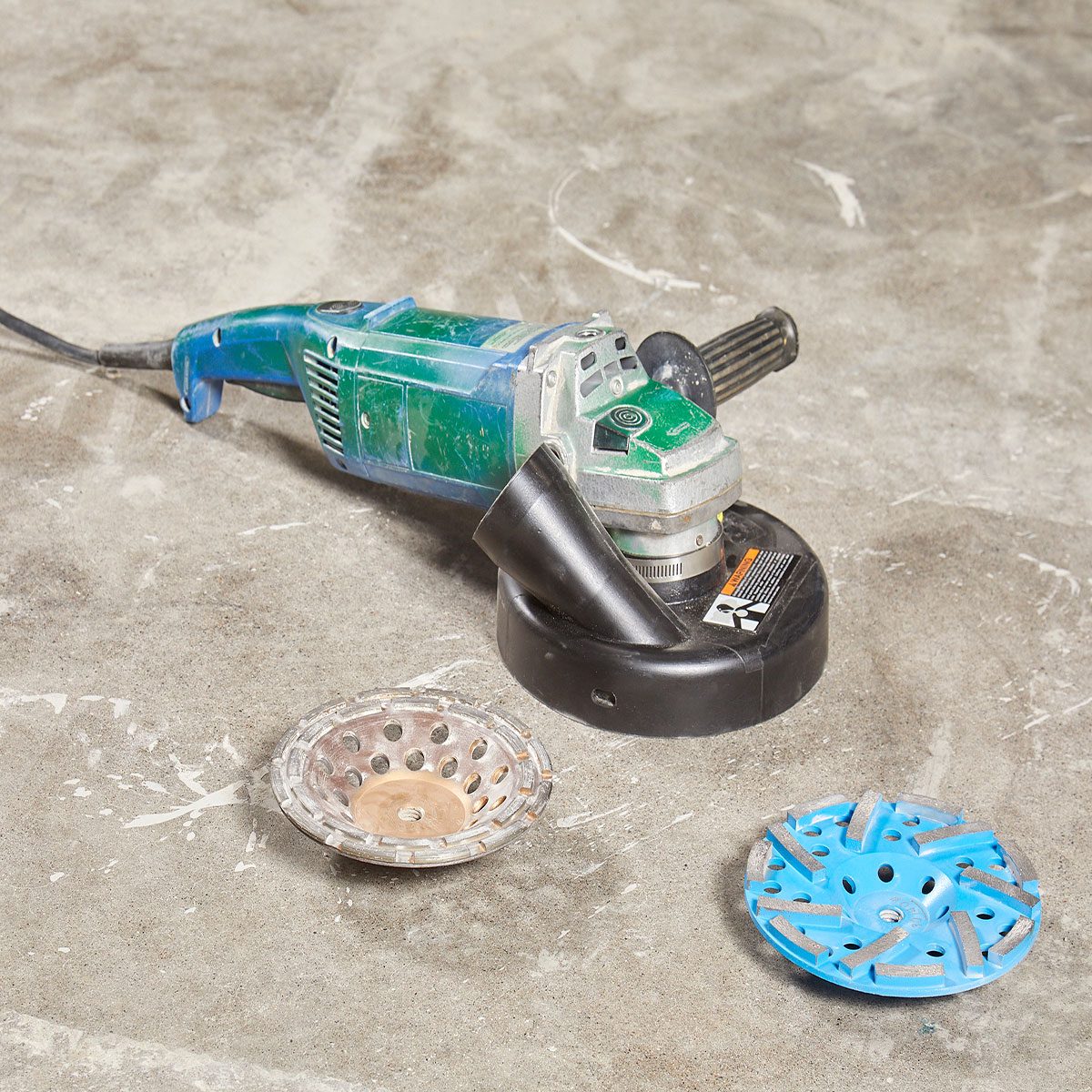 A power tool lies on a concrete surface, with two circular attachments nearby, suggesting preparation for grinding or polishing work.