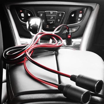 A pair of red and black wires connects to a power outlet in a car, resting on a leather surface near a gear shift and climate controls.