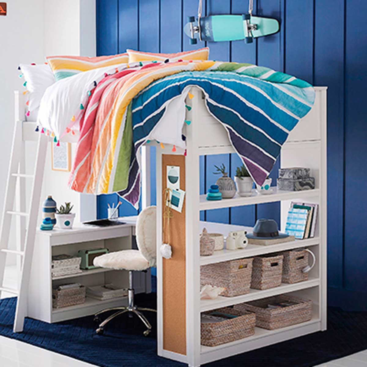 A loft bed displays vibrant, striped bedding above a desk and shelves, set against a blue wall, creating a colorful, organized study space.
