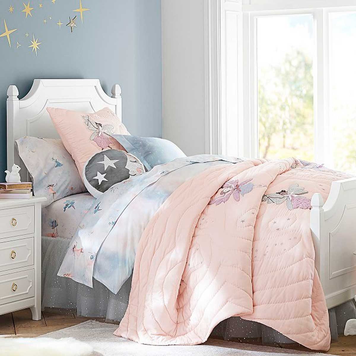 A bed with pastel bedding is neatly arranged, featuring decorative pillows and a quilt, positioned against a light blue wall with star decorations.