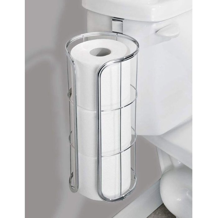 A chrome wire holder contains several rolls of white toilet paper, positioned beside a toilet in a bathroom setting.