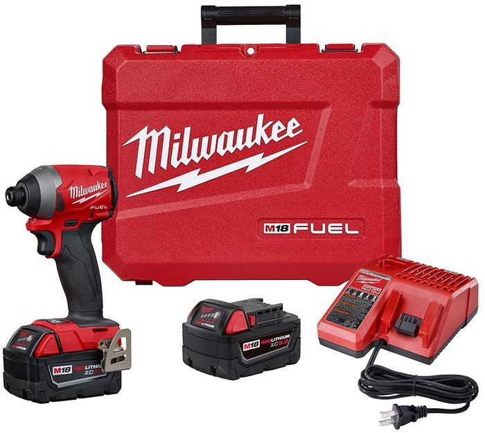 A red power tool sits beside a matching case, two batteries, and a charger, all arranged neatly on a plain background.
