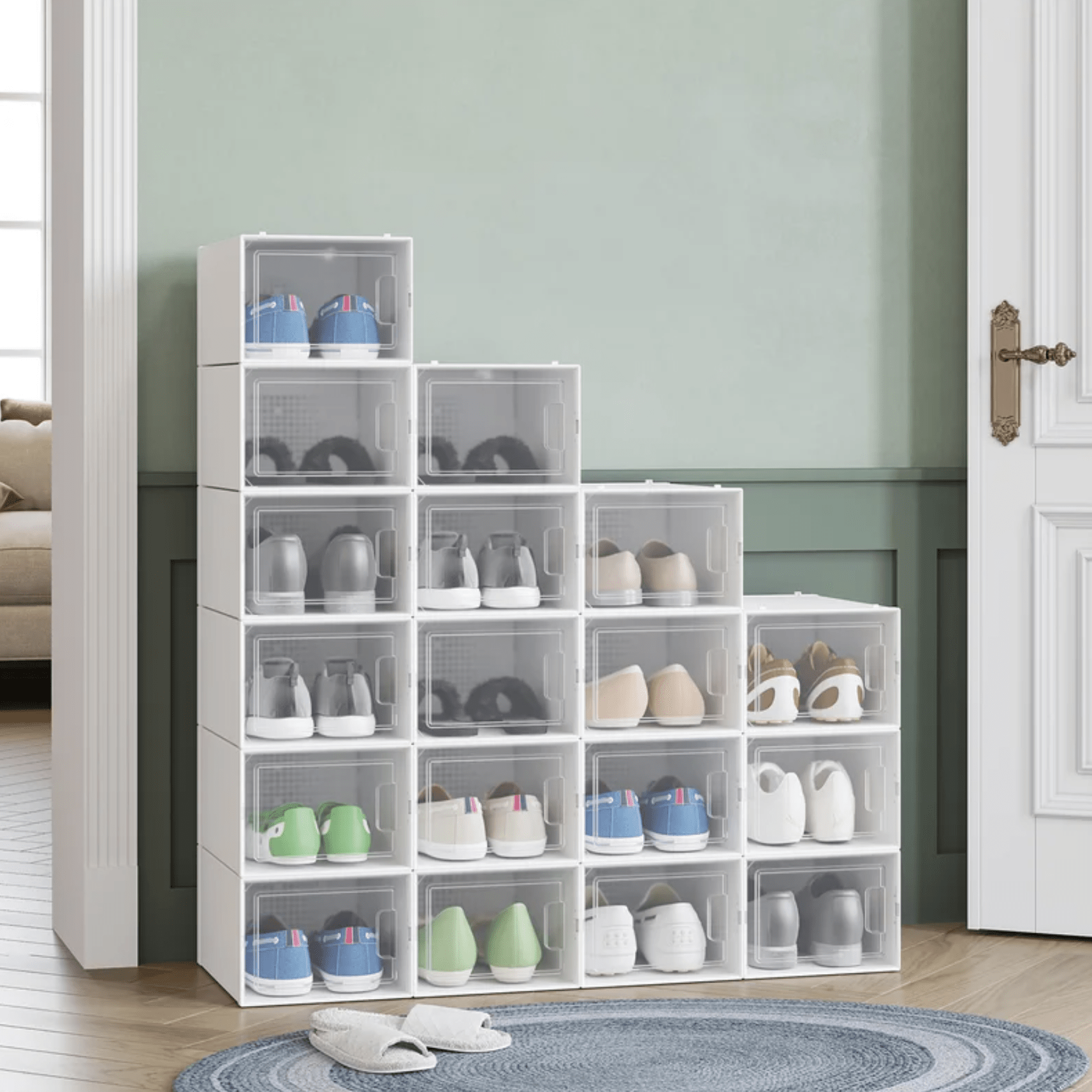 A shoe storage unit displays various types of shoes in transparent boxes, positioned against a light green wall beside a doorway and rug.