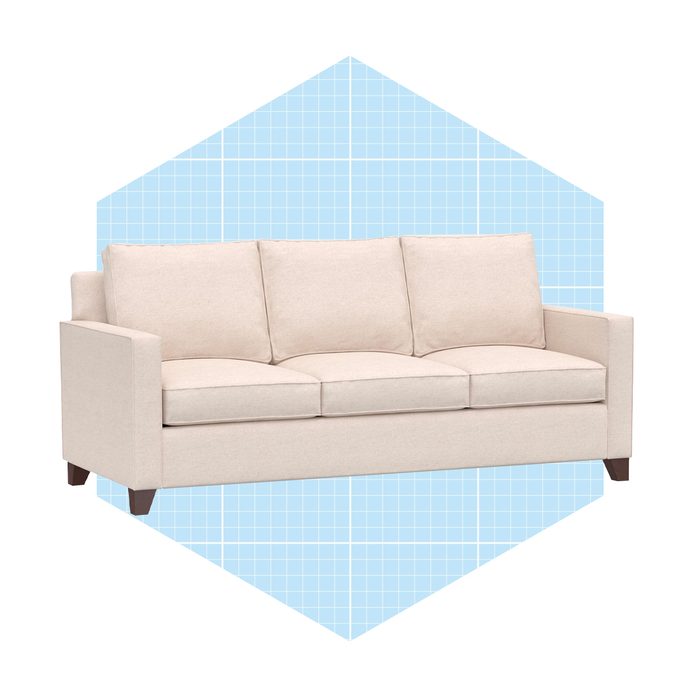 A beige sofa with three cushions sits prominently against a light blue grid-patterned background, creating a modern, minimalistic aesthetic.