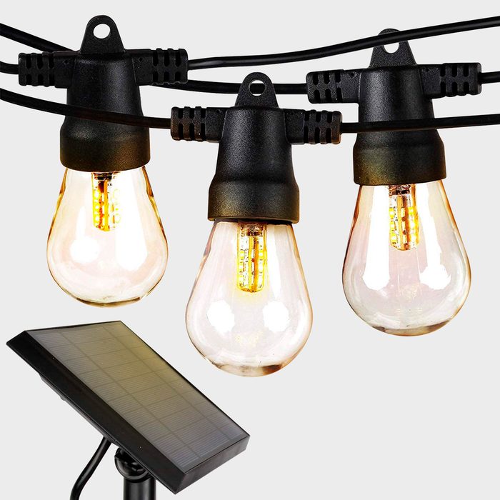 Three light bulbs hang from black wires, illuminated, while a solar panel rests below, likely for powering the lights in an outdoor setting.