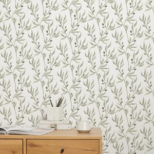 A wooden dresser holds books and a cup, while a patterned wallpaper featuring green branches and leaves decorates the background, creating a serene atmosphere.