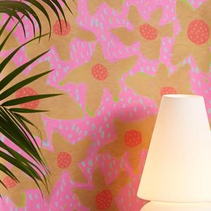 A modern lamp emits soft light, positioned beside a tropical plant, against a vibrant wall covered in pink and yellow floral patterns.