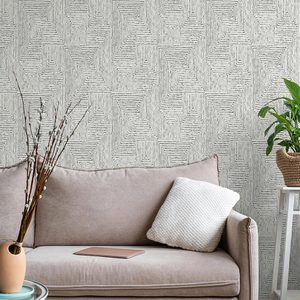 A beige couch with a cushion supports a tablet, while a vase with branches and a potted plant sit nearby against patterned wallpaper.