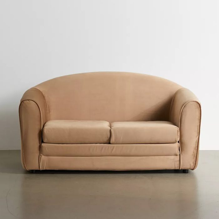 A beige, upholstered couch sits against a plain wall, featuring rounded arms and two comfortable cushions, set on a smooth, light-colored floor.