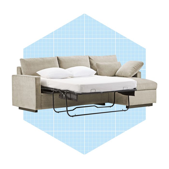 A beige sectional sofa with white cushions is partially converted into a bed, set against a light blue geometric background.