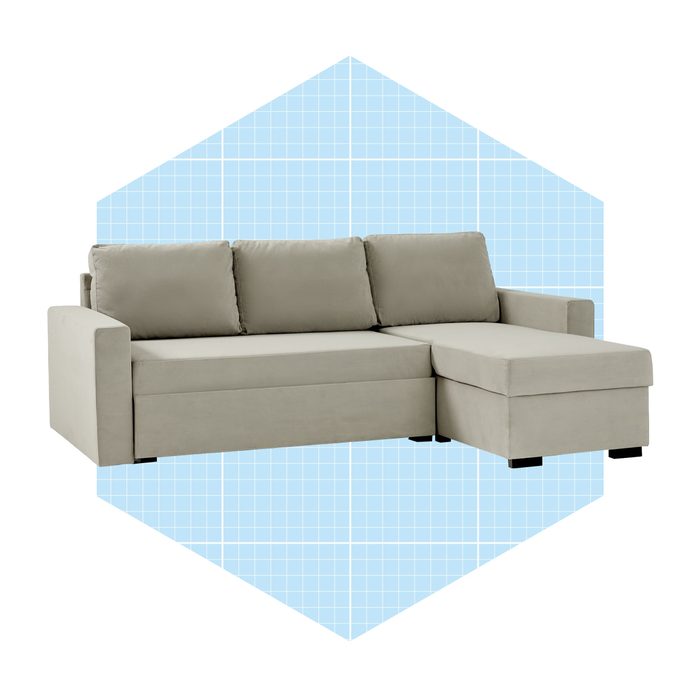 A light gray sectional sofa sits against a blue grid-patterned background, featuring cushioned seats and a chaise lounge extension for comfort.