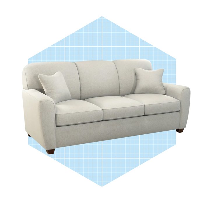 A light gray sofa with two cushions is centered on a blue grid-patterned background, creating a structured and modern aesthetic.