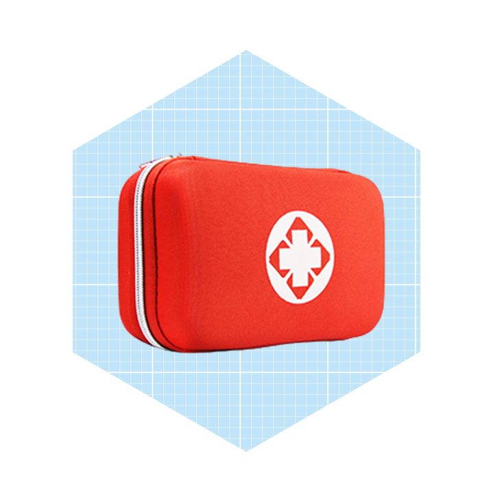 A red first aid kit rests upright, featuring a white cross symbol, set against a light blue grid background.
