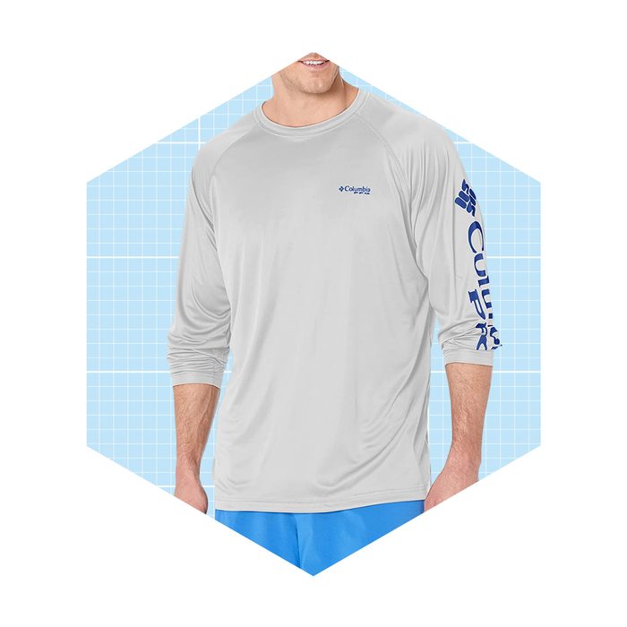 A man wears a light gray long-sleeve shirt with blue lettering, smiling against a light blue grid background. His shirt suggests casual or outdoor activity.