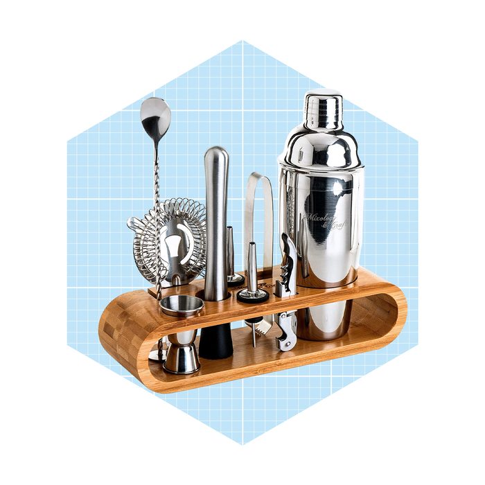 A polished cocktail shaker and various bar tools are arranged on a wooden stand, set against a light blue grid background.