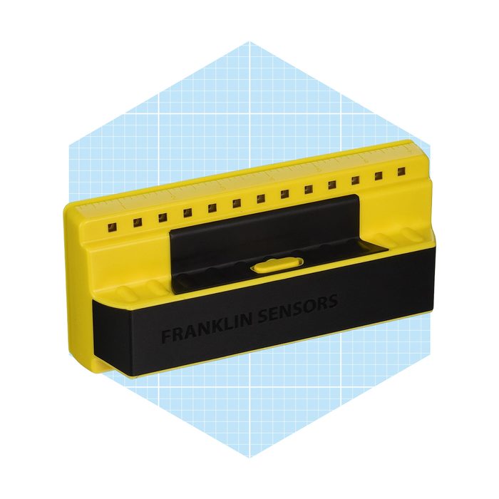 A yellow and black stud finder rests on a light blue grid-patterned background, designed for detecting wall studs during construction or renovation.