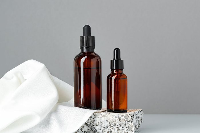 Set of brown glass bottles with essential oils on stand on gray background close up